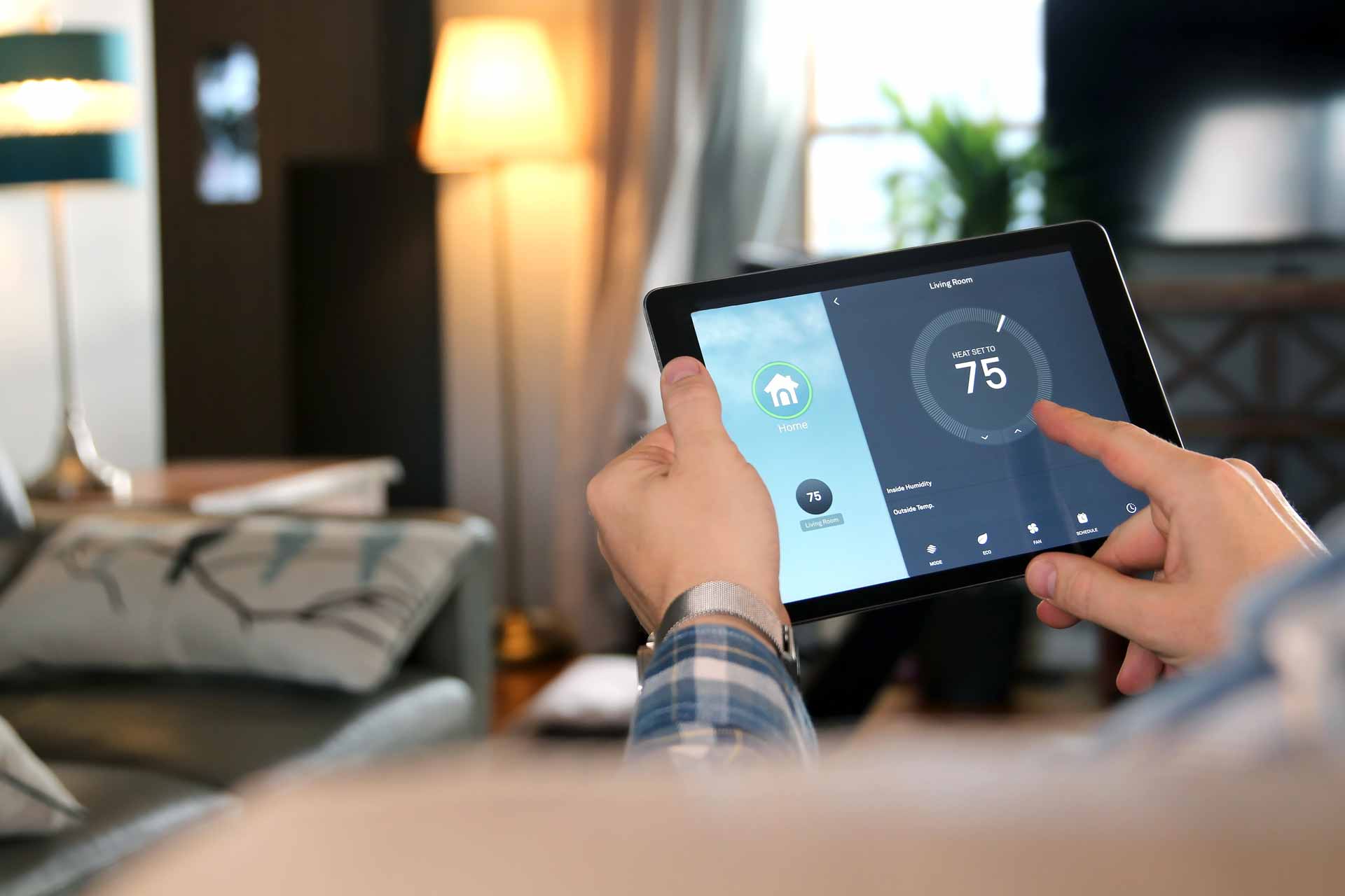 Homeowner controlling smart thermostat from a tablet on their couch